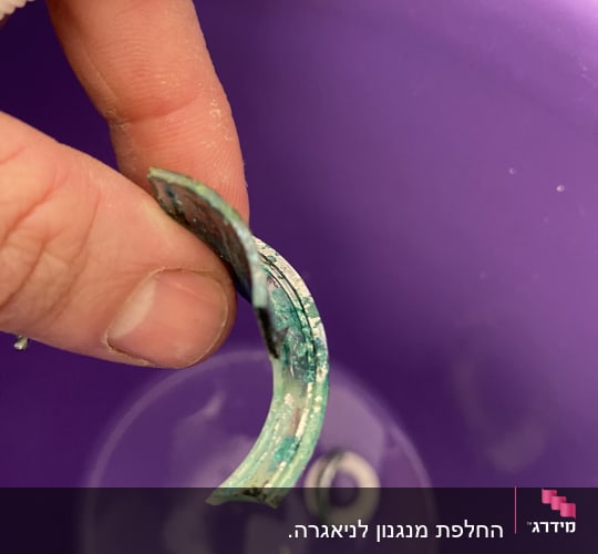 יד מחזיקה חלק צינור מתכת חלוד מעל דלי סגול